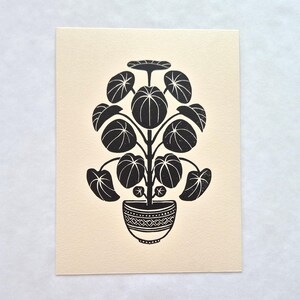 Op de afbeelding: Een zwarte inktblokdruk op crèmekleurig papier met een gestileerde potplant met ronde, geaderde bladeren. De plant staat centraal in een decoratieve kom met een geometrisch patroon van driehoeken en horizontale lijnen.