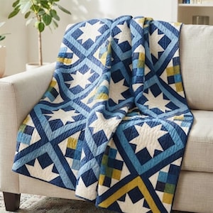 Op de afbeelding: Een gewatteerde plaid met een geometrisch patroon van witte achtpuntige sterren tegen een achtergrond van marineblauwe, lichtblauwe en olijfgroene vierkanten. De stof heeft over het gehele oppervlak zichtbare stiklijnen.