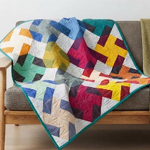 May include: A patchwork quilt featuring a repeating pinwheel pattern in vibrant colors including yellow, magenta, teal, blue, and orange, contrasted with white fabric blocks. The quilt has a teal border and intricate quilted stitching throughout.