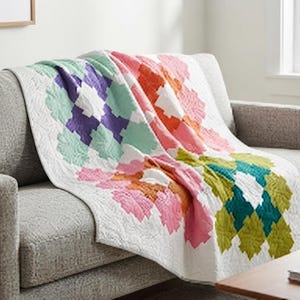 Peut inclure: Une courtepointe avec un fond blanc et un motif géométrique répétitif de formes imbriquées dans des tons de vert menthe, violet, corail, rose, orange, vert lime et sarcelle. Le tissu présente une texture matelassée visible sur toute la surface.