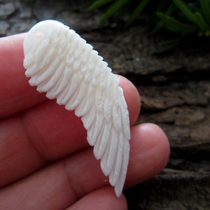 Puede incluir: P&eacute;ndulo de ala de hueso blanco tallado con un agujero en la parte superior para encordar. El ala est&aacute; detallada con plumas talladas.