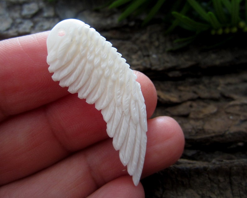 Puede incluir: P&eacute;ndulo de ala de hueso blanco tallado con un agujero en la parte superior para encordar. El ala est&aacute; detallada con plumas talladas.