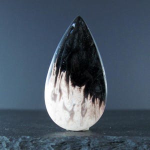 May include: A teardrop-shaped pendant with a black and white marbled design. The top half is solid black, transitioning into a white and brown swirling pattern at the bottom. The pendant is smooth and polished.
