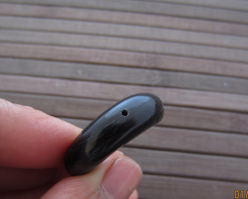 K&ouml;nnte beinhalten: Schwarzer, glatter, ovaler Anh&auml;nger mit einem kleinen Loch in der Mitte.