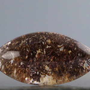 May include: A clear, faceted, teardrop-shaped gemstone with brown and reddish-brown inclusions. The gemstone has a smooth, polished surface.