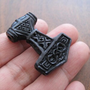 May include: Black wooden pendant carved in the shape of Thor's hammer, Mjolnir, with intricate knotwork and geometric designs.