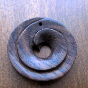 May include: A dark brown wooden pendant with a spiral design. The pendant has a hole at the top for a cord or chain.