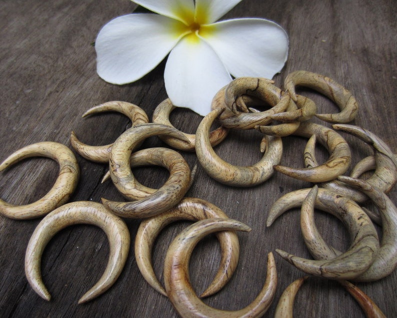 May include: A collection of wooden crescent moon shaped earrings in various shades of brown with natural wood grain patterns.