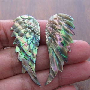 May include: A pair of iridescent abalone shell wings with a green, blue, and purple color scheme. The wings are carved in a detailed feather pattern.