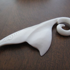 Op de afbeelding: Witte gegraveerde beenhanger met een spiraalvormig ontwerp. De hanger is gevormd als een visstaart met een spiraal aan het einde.