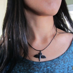 May include: A black cord necklace with a black bird pendant. The bird has outstretched wings.