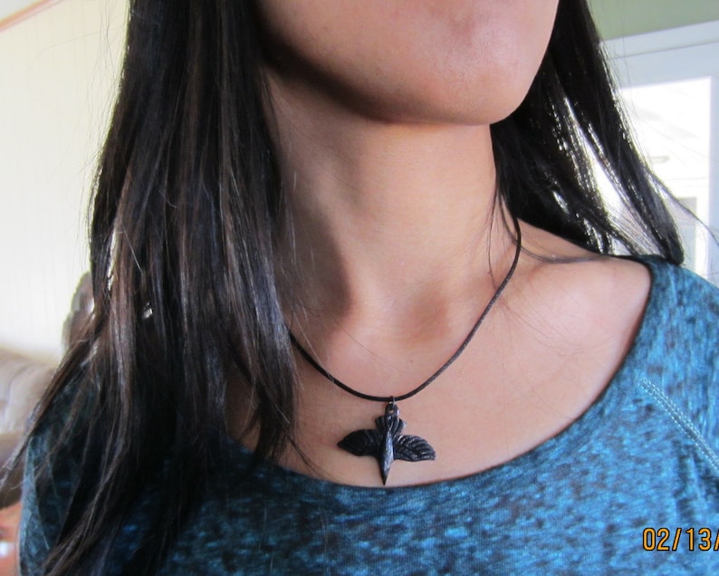 May include: A black cord necklace with a black bird pendant. The bird has outstretched wings.