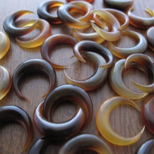 May include: A collection of brown and tan horn crescent shaped rings. The rings are made of polished horn and have a natural, organic look.