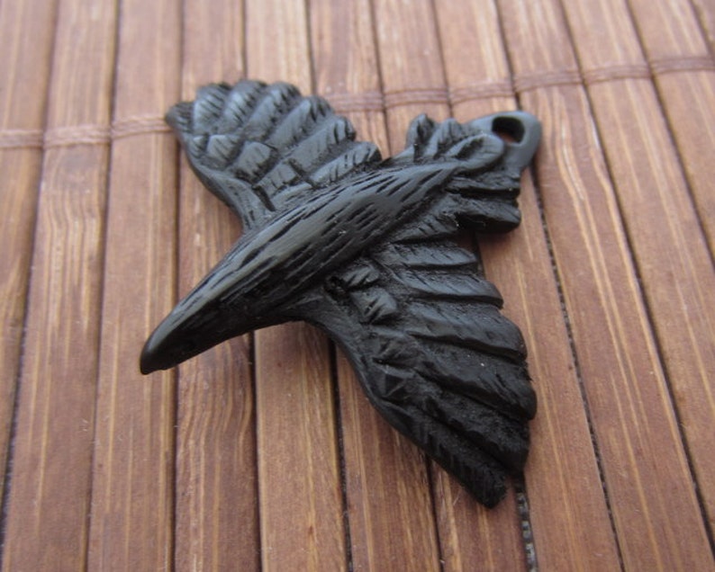 May include: Black raven pendant charm made of polymer clay. The raven is in flight with its wings spread out. The pendant is detailed with textured feathers.