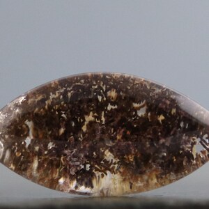 May include: A clear, faceted, teardrop-shaped gemstone with brown and white dendritic inclusions. The gemstone has a smooth, polished surface.