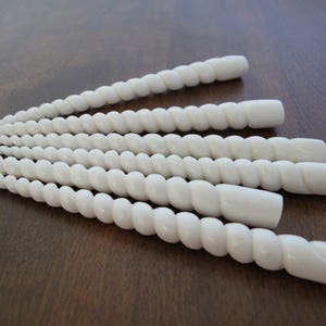 Puede incluir: Seis objetos blancos y retorcidos, que parecen huesos, posiblemente hechos de conchas marinas, dispuestos en fila sobre una superficie de madera.