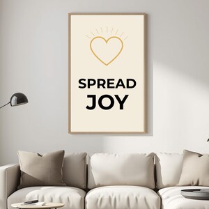 Può includere: Una stampa artistica da parete incorniciata con sfondo color crema presenta un cuore dorato con linee radianti e le parole "SPREAD JOY" in nero. La stampa è esposta sopra un divano bianco con cuscini dai colori neutri. La frase "Printable Wall Art - Instant Download" è in basso.