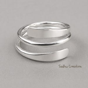 May include: A silver wrap ring with a spiral design. The ring has a smooth, polished finish and a modern, minimalist aesthetic. The ring is a piece of jewellery.