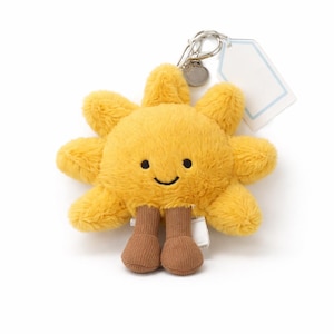 May include: A plush yellow sun-shaped keychain with a smiling face and brown feet. The keychain has a silver clasp and a blank tag attached. The sun has eight rays and a soft, fuzzy texture.