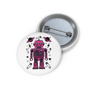 May include: A white button with a pink robot illustration. The robot has a leopard print design and is surrounded by planets, lightning bolts, safety pins, and stars. The button has a metal pin back.