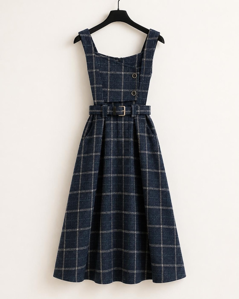 May include: A dark blue sleeveless dress featuring a white grid pattern, a square neckline, and a fitted bodice with two buttons. The dress includes a matching fabric belt with a buckle at the waist and a flared skirt that falls below the knee.