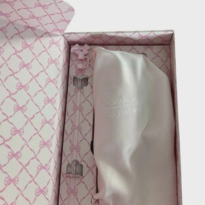 Puede incluir: Una caja de regalo rosa con un patr&oacute;n de lazo contiene una botella de agua rosa y una bolsa con cord&oacute;n a juego. El interior de la caja presenta un dise&ntilde;o de lazo repetido. La botella de agua tiene una pajita transparente y una parte superior en forma de lazo rosa. La bolsa tiene el texto "STANLEY LOVESHACKFANCY".