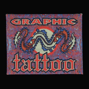 Peut inclure: Un écusson tissé rectangulaire présentant le mot GRAPHIC en lettres noires grasses en haut et le mot tattoo dans une police gothique rouge stylisée en bas. Un emblème circulaire blanc central représente un dragon bleu et orange en pose serpentine.