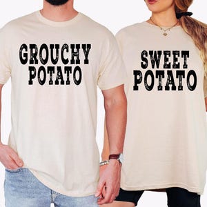 May include: Two cream-colored short-sleeve t-shirts. The left shirt features the black text "GROUCHY POTATO" in a distressed font. The right shirt features the black text "SWEET POTATO" in the same distressed font style.