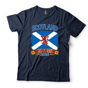 May include: Navy blue t-shirt featuring the Scottish flag with a white X on a blue background and a red lion in the center. The text "SCOTLAND" is above the flag, and "WORLD CUP 2026" is below.