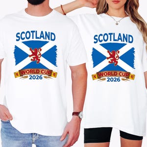 May include: White t-shirts with a graphic featuring the Scottish flag, a red lion, and the text "SCOTLAND WORLD CUP 2026" in blue and gold. The design is centered on the front of the shirts, suitable for sports fans.