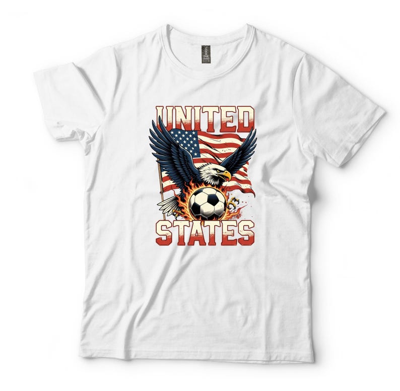 K&ouml;nnte beinhalten: Ein wei&szlig;es Kurzarm-T-Shirt mit einem Grafikdruck eines Wei&szlig;kopfseeadlers mit ausgebreiteten Fl&uuml;geln &uuml;ber einem von Flammen umgebenen Fu&szlig;ball. Dahinter ist eine wehende amerikanische Flagge zu sehen. Der Text UNITED STATES steht in roten Buchstaben.