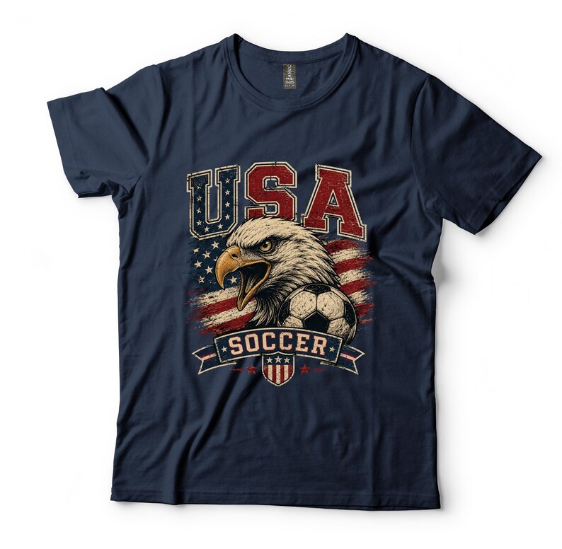 Puede incluir: Una camiseta azul marino de manga corta con un estampado gr&aacute;fico de un &aacute;guila calva, un bal&oacute;n de f&uacute;tbol y la bandera estadounidense. El texto USA y SOCCER est&aacute; impreso en una fuente desgastada. El dise&ntilde;o incluye un peque&ntilde;o emblema de escudo.