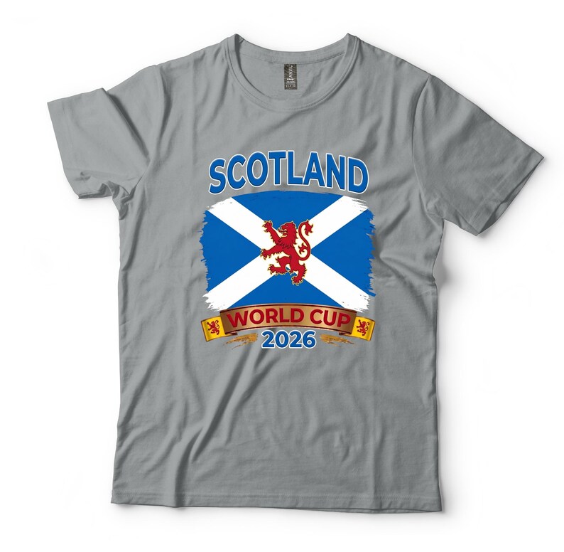 May include: Gray t-shirt featuring the word "SCOTLAND" above a blue and white flag design with a red lion emblem. Below the flag is "WORLD CUP 2026" in white text on a gold banner. A casual tee for fans.