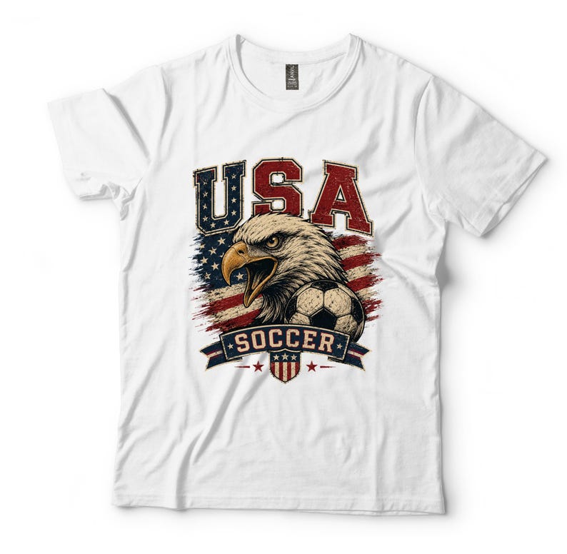 Puede incluir: Una camiseta blanca de manga corta con un estampado gr&aacute;fico de una cabeza de &aacute;guila calva, un bal&oacute;n de f&uacute;tbol y el texto USA SOCCER. El dise&ntilde;o incorpora un fondo de bandera estadounidense desgastada en rojo, blanco y azul con un escudo.