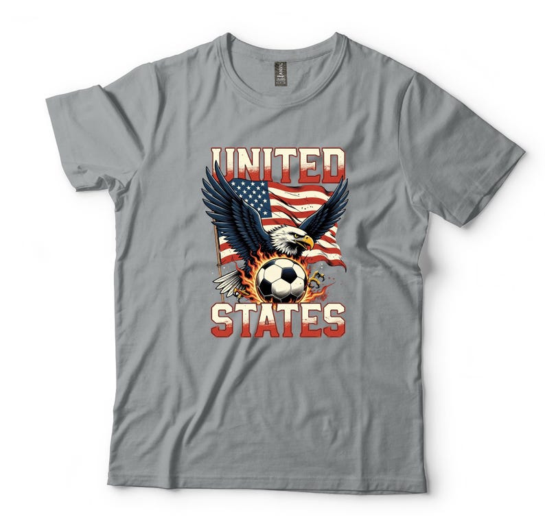 K&ouml;nnte beinhalten: Ein graues T-Shirt mit einer Grafik eines Wei&szlig;kopfseeadlers mit ausgebreiteten Fl&uuml;geln &uuml;ber einem von Flammen umgebenen Fu&szlig;ball. Hinter dem Adler ist eine wehende amerikanische Flagge zu sehen. Der Text UNITED STATES ist in fetten rot-wei&szlig;en Blockbuchstaben gedruckt.