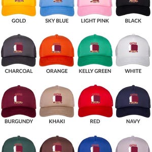 May include: A collection of trucker hats in various colors, each featuring the word "QATAR" and a flag design. Colors include gold, sky blue, light pink, black, charcoal, orange, kelly green, white, burgundy, khaki, red, navy, dark green, dark brown, royal blue, and grey.