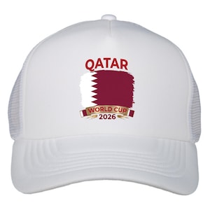 May include: White trucker hat featuring the word "QATAR" in maroon above a maroon and white graphic of the Qatar flag. Below the flag is a banner that reads "WORLD CUP 2026" in gold lettering.