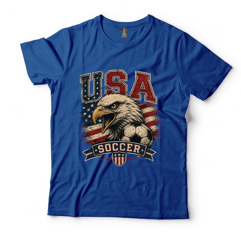 Puede incluir: Una camiseta de manga corta color azul real con un estampado gr&aacute;fico de un &aacute;guila calva, un bal&oacute;n de f&uacute;tbol y la bandera estadounidense. El texto USA aparece en rojo y blanco sobre el &aacute;guila, y la palabra SOCCER en blanco sobre una banda azul.
