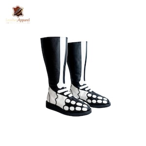 May include: A pair of knee-high boots featuring a black base with a white skeleton bone print. The design includes a vertical bone pattern running up the shaft and circular bone shapes across the foot area, finished with a solid black flat sole.