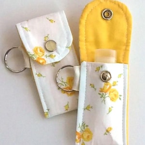 May include: Two fabric cases with key rings. The cases are white with a yellow rose pattern and yellow lining. Each case has a snap closure. One case is open, revealing a small bottle.