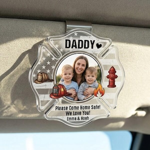 May include: A clear acrylic car visor clip in the shape of a firefighter's Maltese cross. The clip features a family photo, the word "DADDY", and the text "Please Come Home Safe! We Love You! Emma & Noah". Decorative elements include a fire helmet, a fire hydrant, and flames.