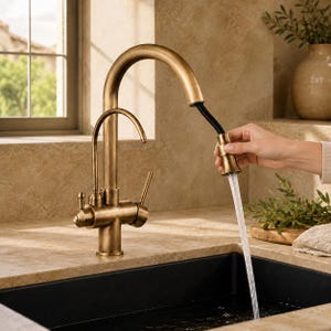 Peut inclure: Un robinet de cuisine en bronze avec un bec en arc de cercle et un pulvérisateur extractible. Le robinet est monté sur un comptoir beige au-dessus d'un évier noir. L'eau coule du pulvérisateur. Le robinet a un design classique.