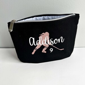 Peut inclure: Pochette zippée en toile noire avec une silhouette rose d'un joueur de hockey et le nom "Addison" en lettres blanches avec le numéro "9" sous le joueur.