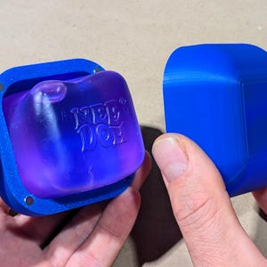 May include: A blue 3D-printed square container with a magnetic lid, featuring a translucent purple insert with the embossed text "YEE DOT" on the front. The container consists of two separate parts, a base holding the purple insert and a solid blue lid.