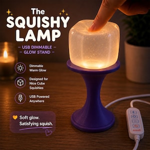 May include: A glowing, cube-shaped lamp with a purple base and a USB power cord. The lamp is labeled "The Squishy Lamp" and features dimmable warm light. The design is intended for use with Nice Cube Squishies.