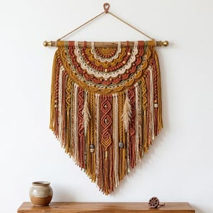 May include: A handcrafted macrame wall hanging in warm tones of mustard, cream, and rust. The textile art piece features intricate knotting, wooden beads, and decorative feathers, suspended from a wooden dowel. This bohemian-style wall decor adds texture and visual interest.