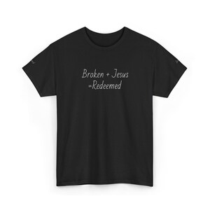 Op de afbeelding: Zwart T-shirt met de handgeschreven tekst "Broken + Jesus = Redeemed". Het shirt heeft een ronde hals en korte mouwen. De tekst is wit.