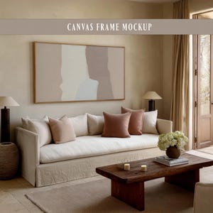 May include: A living room scene featuring a large canvas art piece with a neutral color palette. A white sofa with several pillows in shades of pink and brown sits below the artwork. A wooden coffee table and a woven basket add to the room's decor.