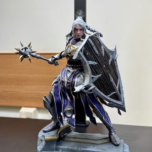 May include: A detailed fantasy figurine of a warrior with silver hair, wearing purple and silver armour. The figure holds a spiked mace in one hand and a large, dark wooden shield with silver metal trim in the other, standing on a stone-like base.