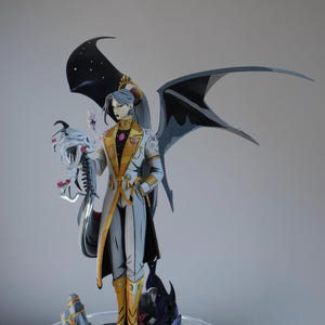 Può includere: Statuetta dettagliata di un personaggio con pelle grigia, lunghi capelli grigi e grandi ali nere. Il personaggio indossa un cappotto bianco e oro, stivali dorati e tiene in mano un oggetto a forma di teschio. La base è un paesaggio roccioso.